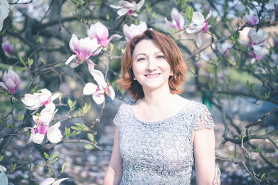 Cheerful middle aged armenian woman in an elegant dress under the magnolia blooming tree. spring par