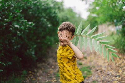 A six-year-old boy runs with green leaves in his hands in the countryside.