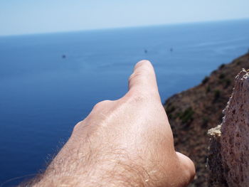 Close-up of hand over sea against sky