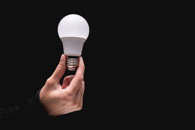 Close-up of hand holding light bulb against black background