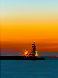 Illuminated lighthouse by sea against sky during sunset