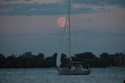 Sailboat sailing on river against sky during sunset