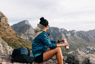 Young man sitting on mountain against sky