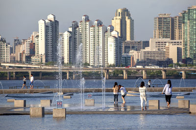 People enjoying in fountain against urban skyline