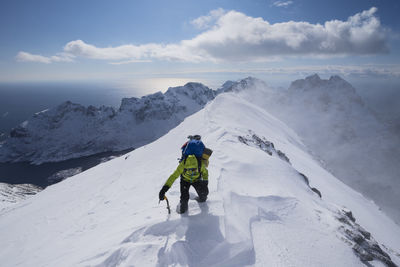 Female hiker aproaching summit of mengensdalstind in deep snow and high wind, moskenesøy, lofoten islands, norway