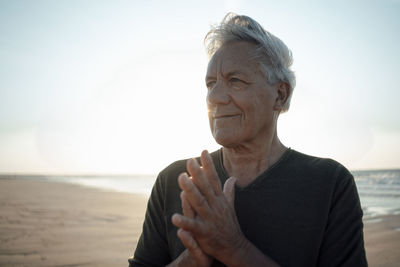 Smiling senior man with hands clasped at beach