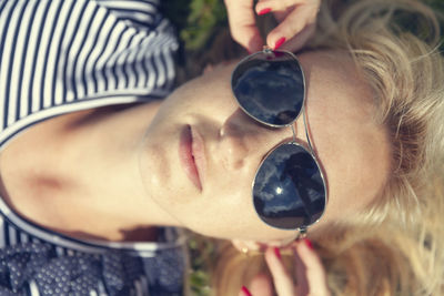 Young millennial woman wearing sunglasses laying on the grass looking up