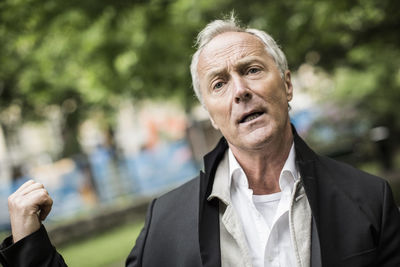 Mature businessman looking away while gesturing in park