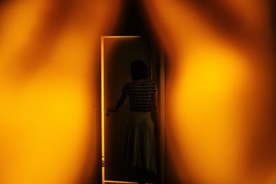 Rear view of man standing against illuminated orange wall