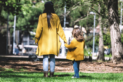 Rear view of mother and daughter holding hands while standing on field in park