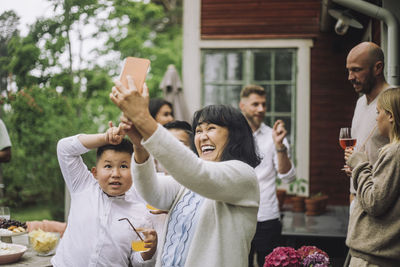 Happy grandmother taking selfie through smart phone with grandchildren at party