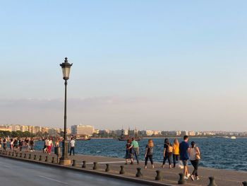 People on street by sea against clear sky