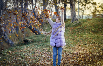 Young woman playing with dry leaves on field during autumn