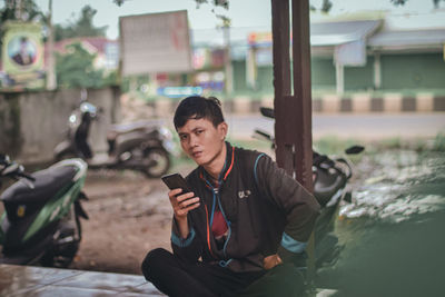 Young woman using mobile phone while sitting in city