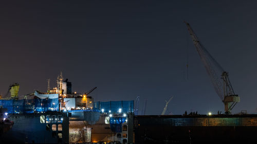 Cranes at harbor against clear sky at night