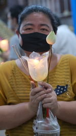 Portrait of woman wearing mask holding candle outdoors