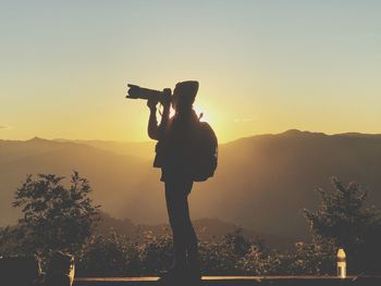 Man photographing at camera against sky during sunset