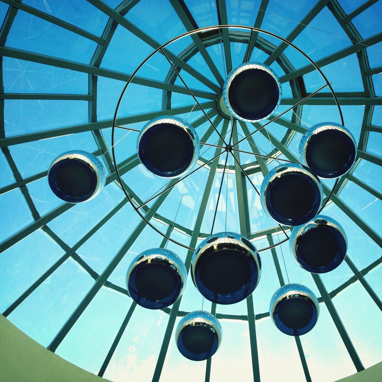 low angle view, ceiling, circle, geometric shape, sky, indoors, metal, directly below, lighting equipment, built structure, architecture, electricity, blue, technology, no people, day, pattern, hanging, backgrounds, cloud - sky