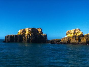 Rock formation in sea against clear blue sky