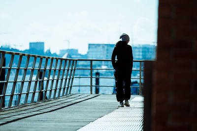 Rear view of silhouette man walking on railing against sky