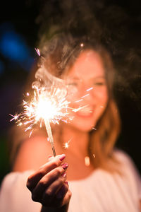 Midsection of woman holding sparkler at night