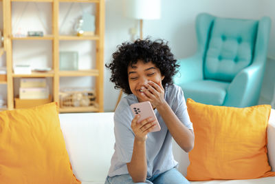 Young woman using mobile phone while sitting on bed at home