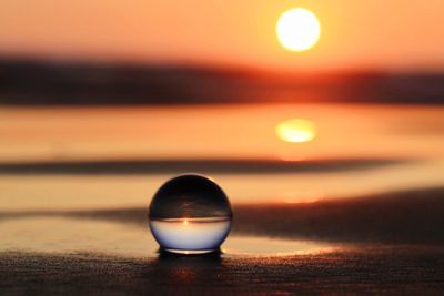 Close-up of glass ball on beach against sky during sunset