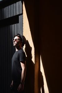 Side view of young man standing against wall