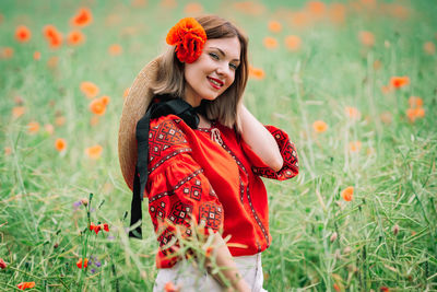 Portrait of young woman with red flowers in field