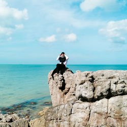 Rear view of woman sitting on rock at beach against sky