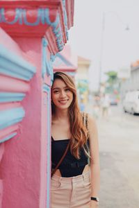 Portrait of young woman standing by wall in city