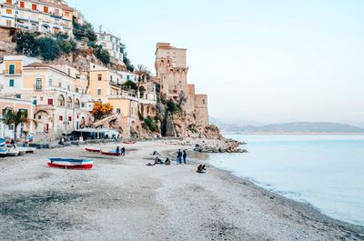 People on beach by buildings in city against clear sky