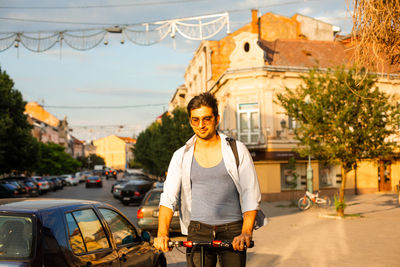 Portrait of young man riding push scooter on street