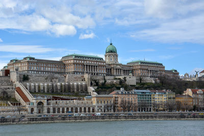 Danube river by buildings and buda castle against cloudy sky