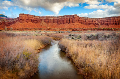 Water amidst grass against rock formation and sky