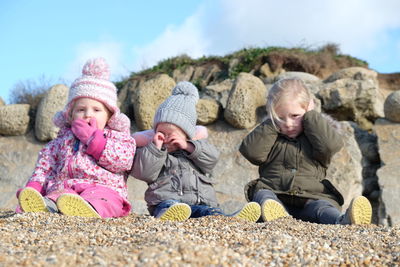 Happy friends sitting on rock against sky