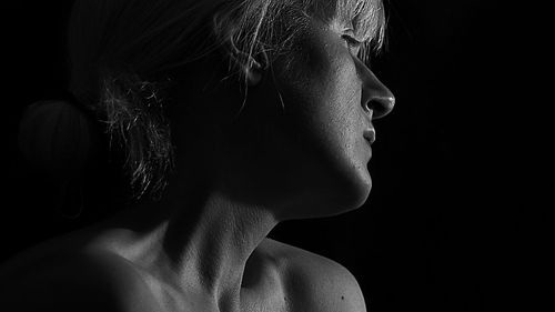 Close-up of woman looking away against black background