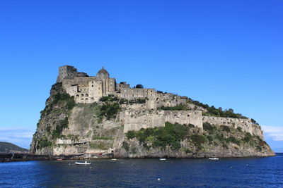 Castle by sea against clear blue sky