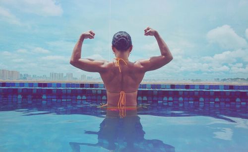 Rear view of woman flexing muscles while standing in swimming pool