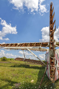 A part of an abandoned aircraft plane standing in the field against the cloudy blue sky.