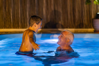 Grandfather and grandson playing in a swimming pool at night