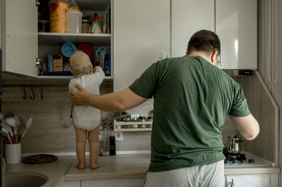 Baby girl standing on kitchen counter with father making coffee