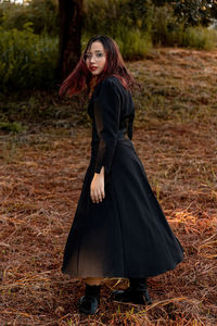 Portrait of teenager girl standing on grass against tree