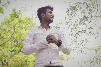 Young man looking away while standing against trees