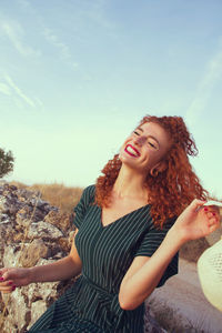 Beautiful young woman sitting against sky