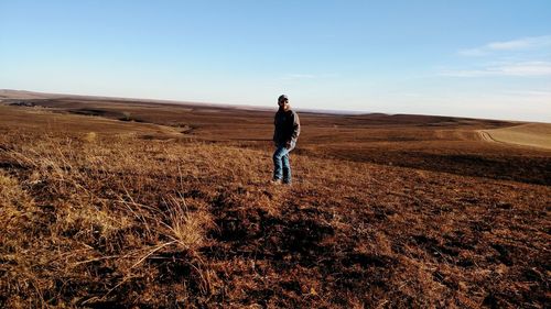 Rear view of man walking on field against sky