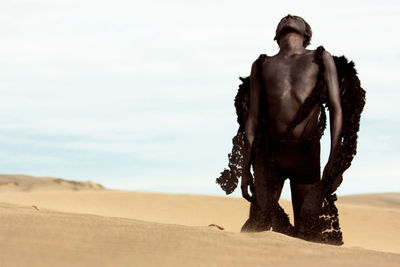 Teenage boy in costume on desert against sky