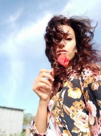 Low angle portrait of beautiful woman holding rose against sky