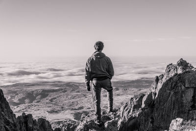Rear view of man standing on rock against sky