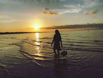 Silhouette woman standing at beach against sky during sunset